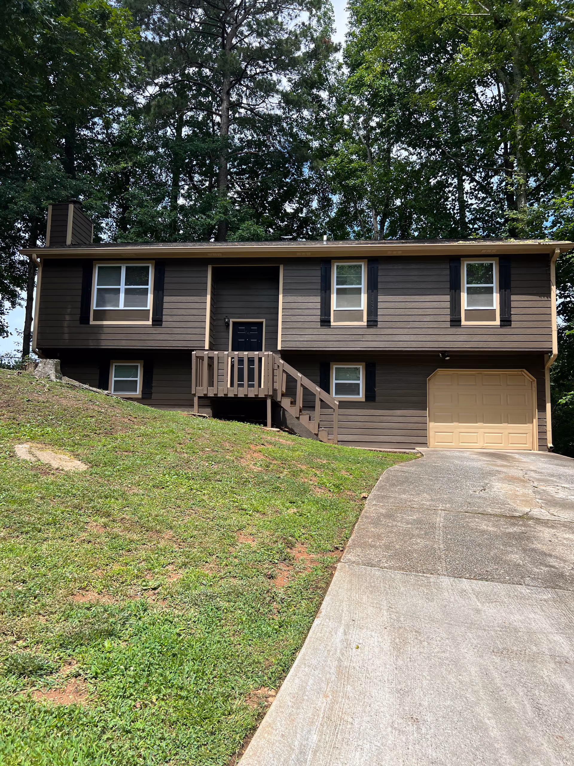 Brown two-story house with front stairs and attached garage among trees.