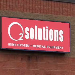 Red sign reading Qsolutions on brick exterior wall, advertising home oxygen and medical equipment.