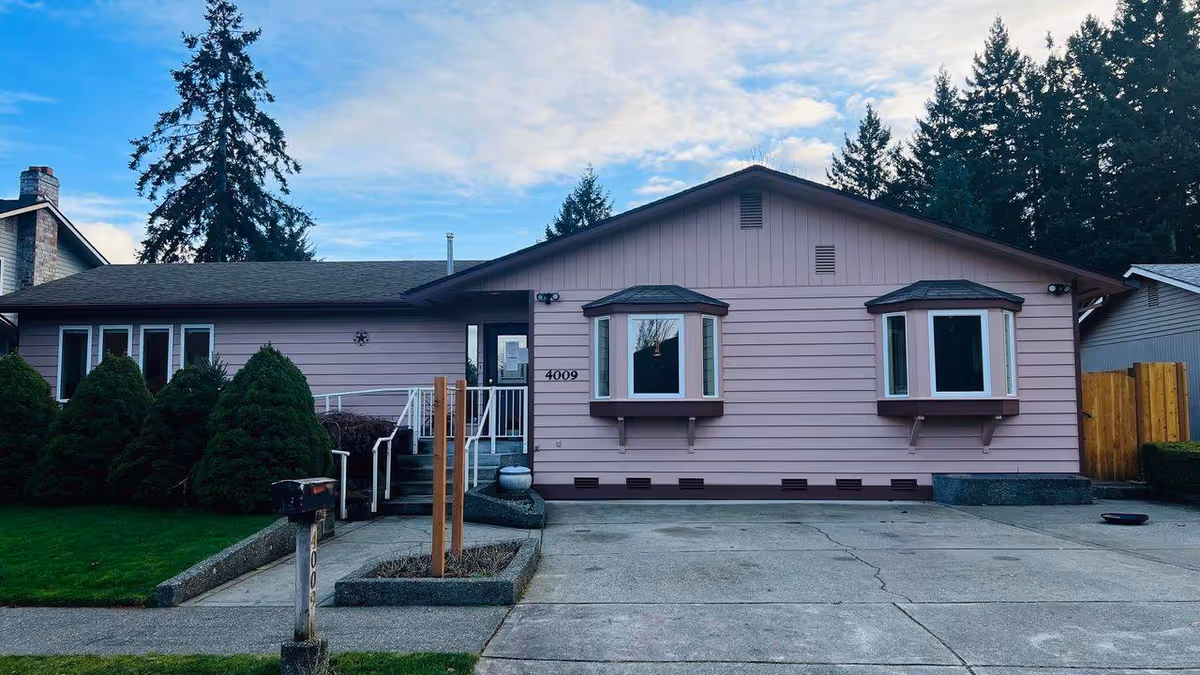 Front view of a pink, single-story house with bay windows and a driveway.