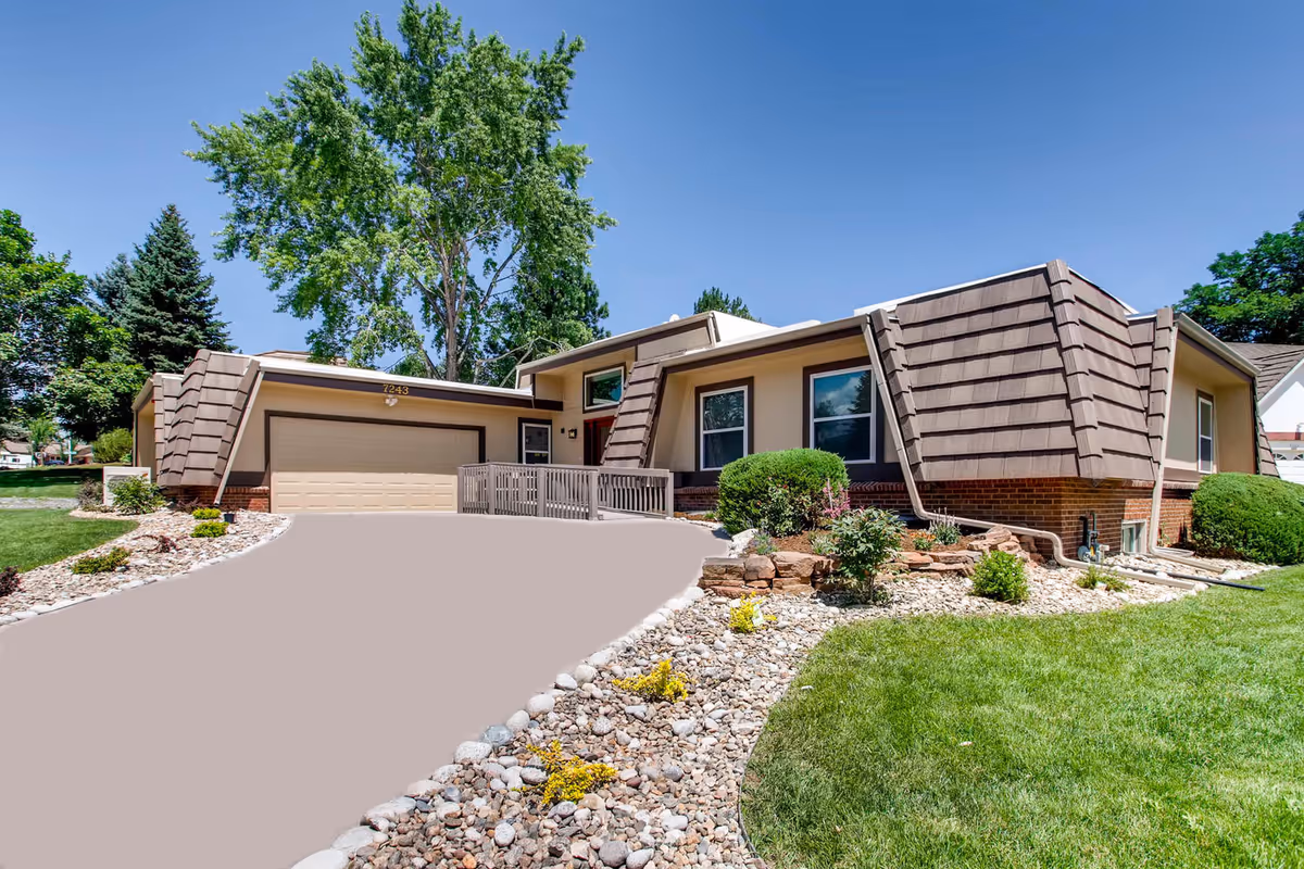 Front exterior of a single-story assisted living building with a two-car garage, landscaped rock beds, and a paved driveway.
