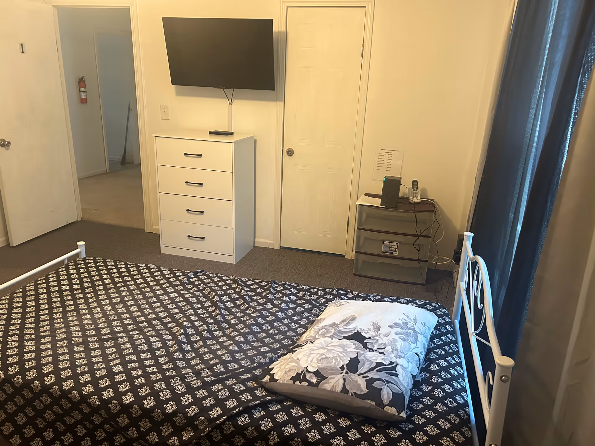 Furnished bedroom with a bed, dresser, mounted TV, and doorway.