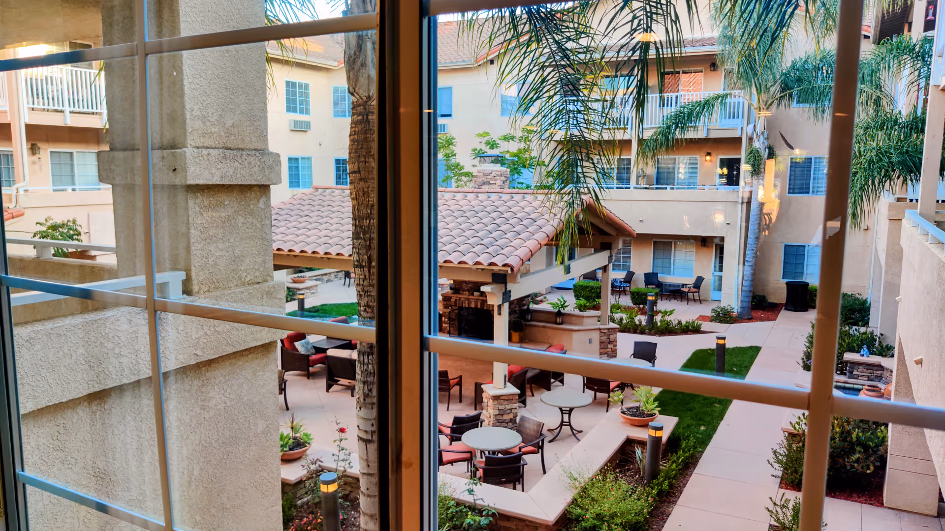Outdoor courtyard at Atria Las Posas with palm trees, patio seating, and walking paths.