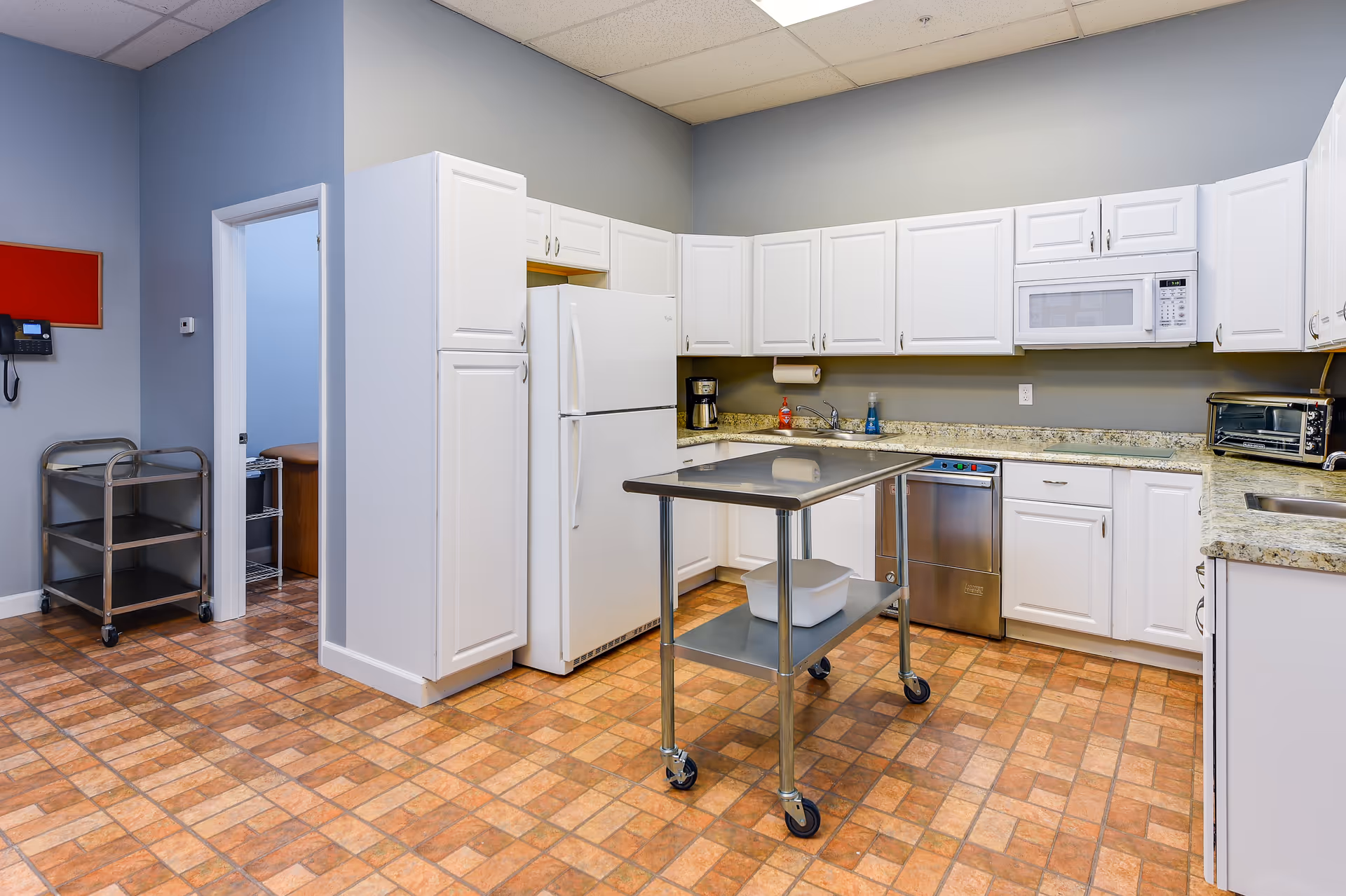 A bright communal kitchen with white cabinets, appliances, and a rolling prep cart.