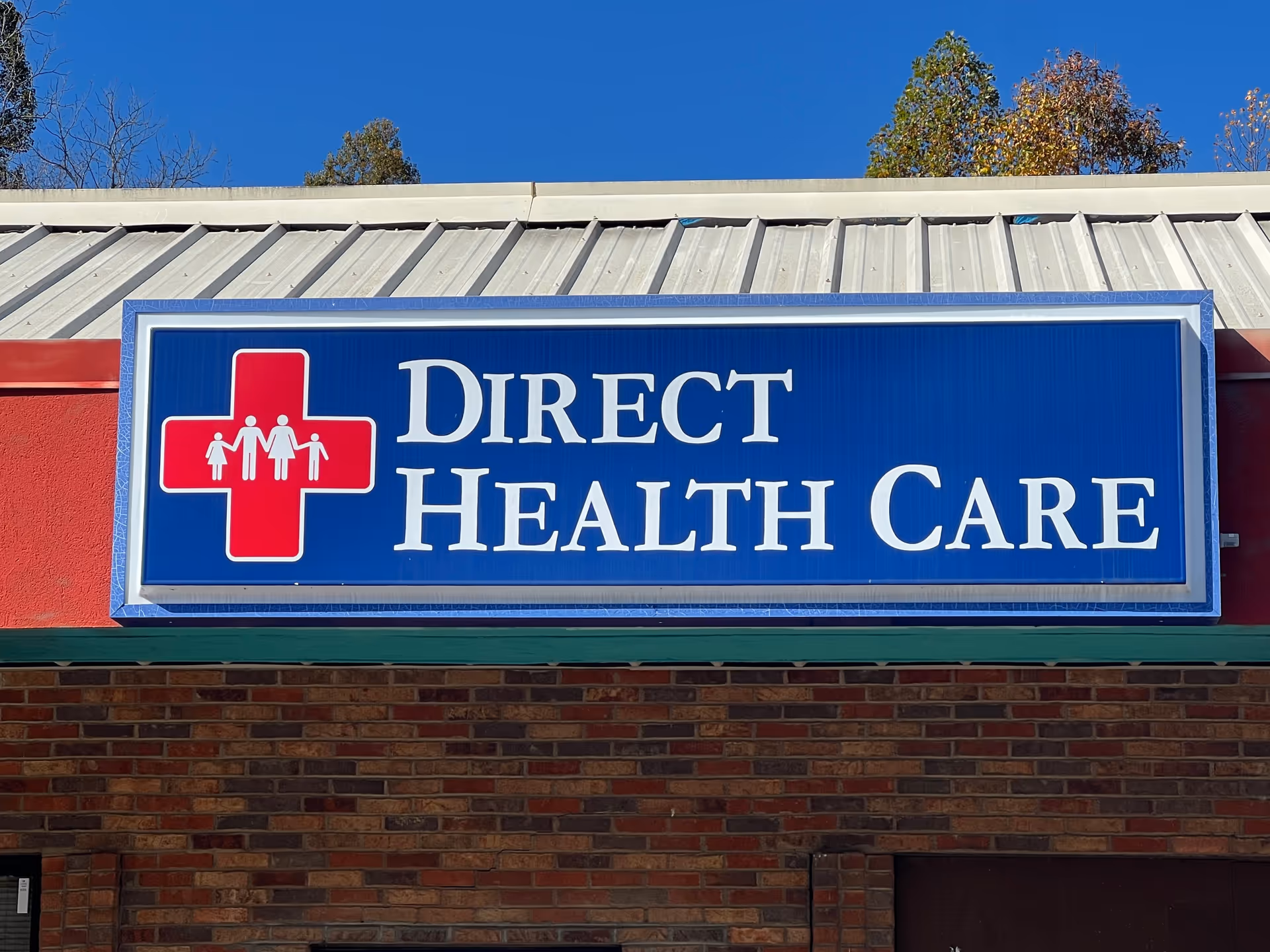 Blue Direct Health Care sign with red medical cross on brick building exterior