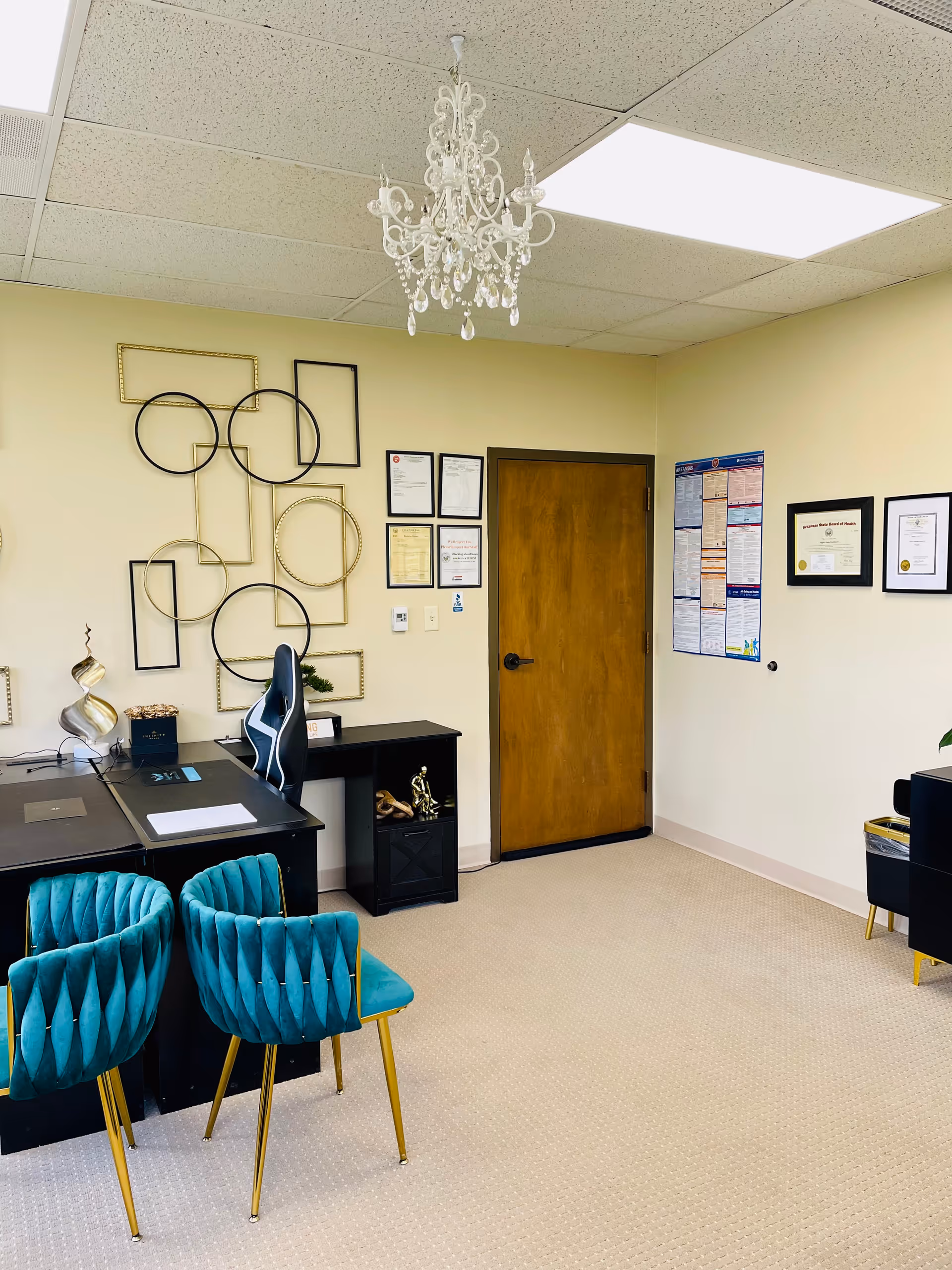 Interior office area with desk, turquoise chairs, chandelier, and framed wall art.