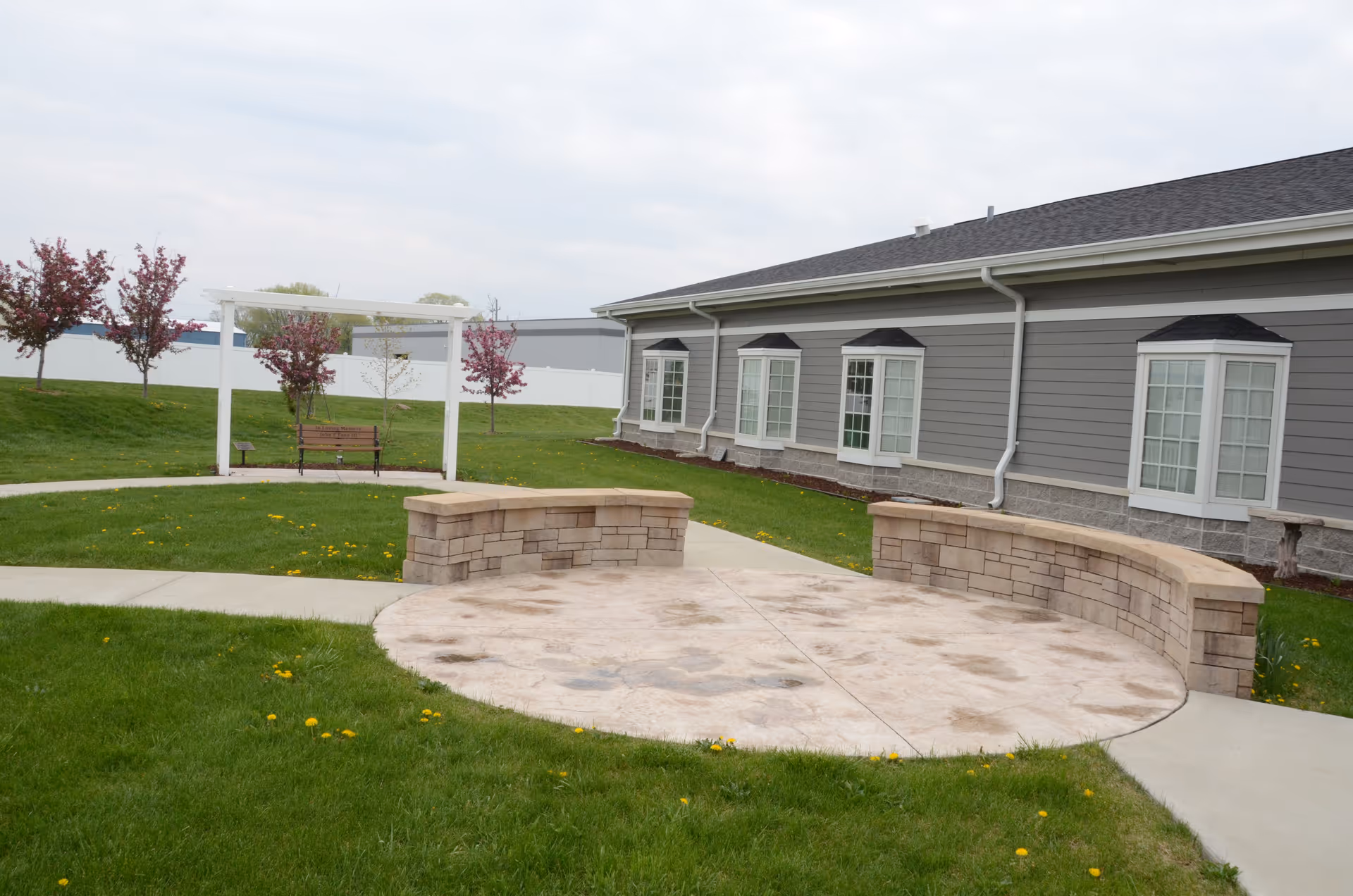 Outdoor view of a senior living facility with curved stone benches and green lawn.