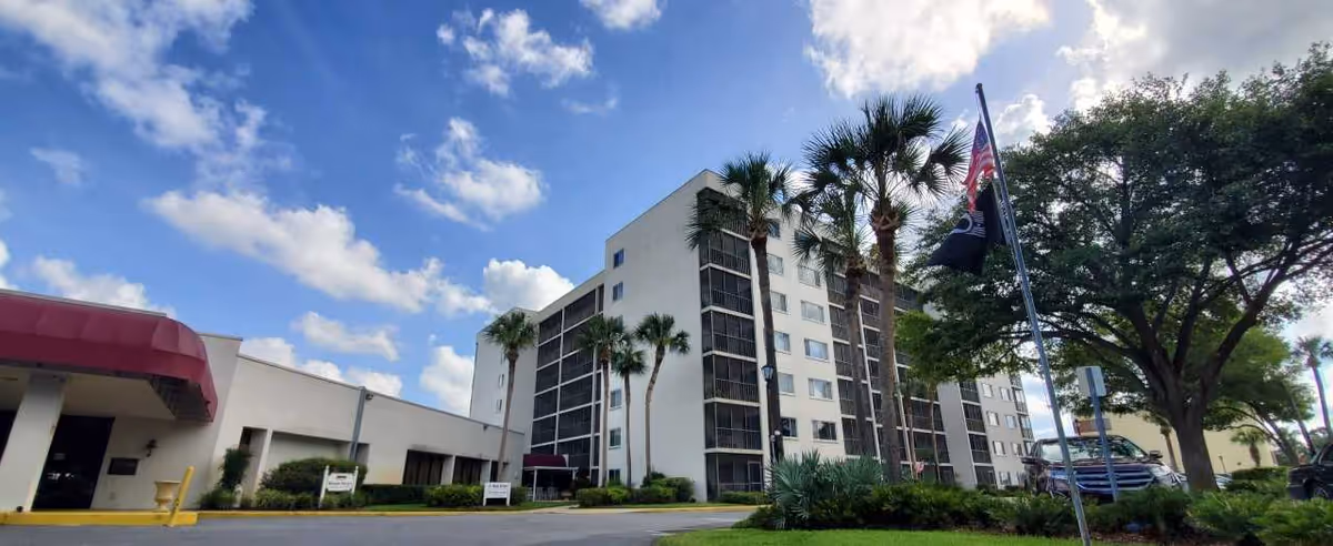 Exterior view of a multi-story senior living building with palm trees and a flag.