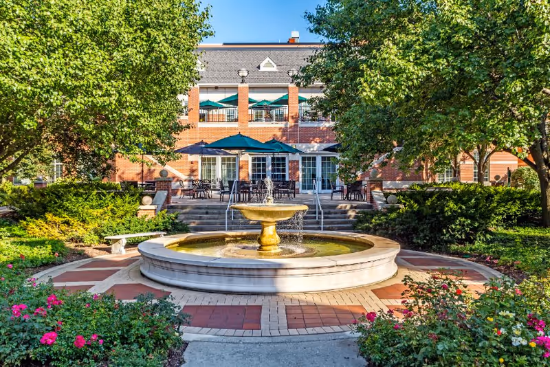Landscaped courtyard with a central fountain and outdoor seating in front of a brick building.