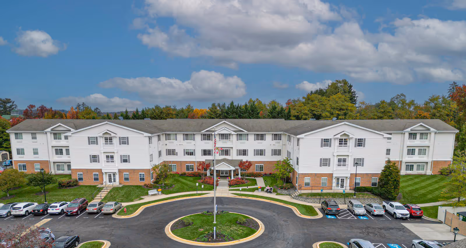 A large white multi-wing senior living building with a circular driveway and parking.