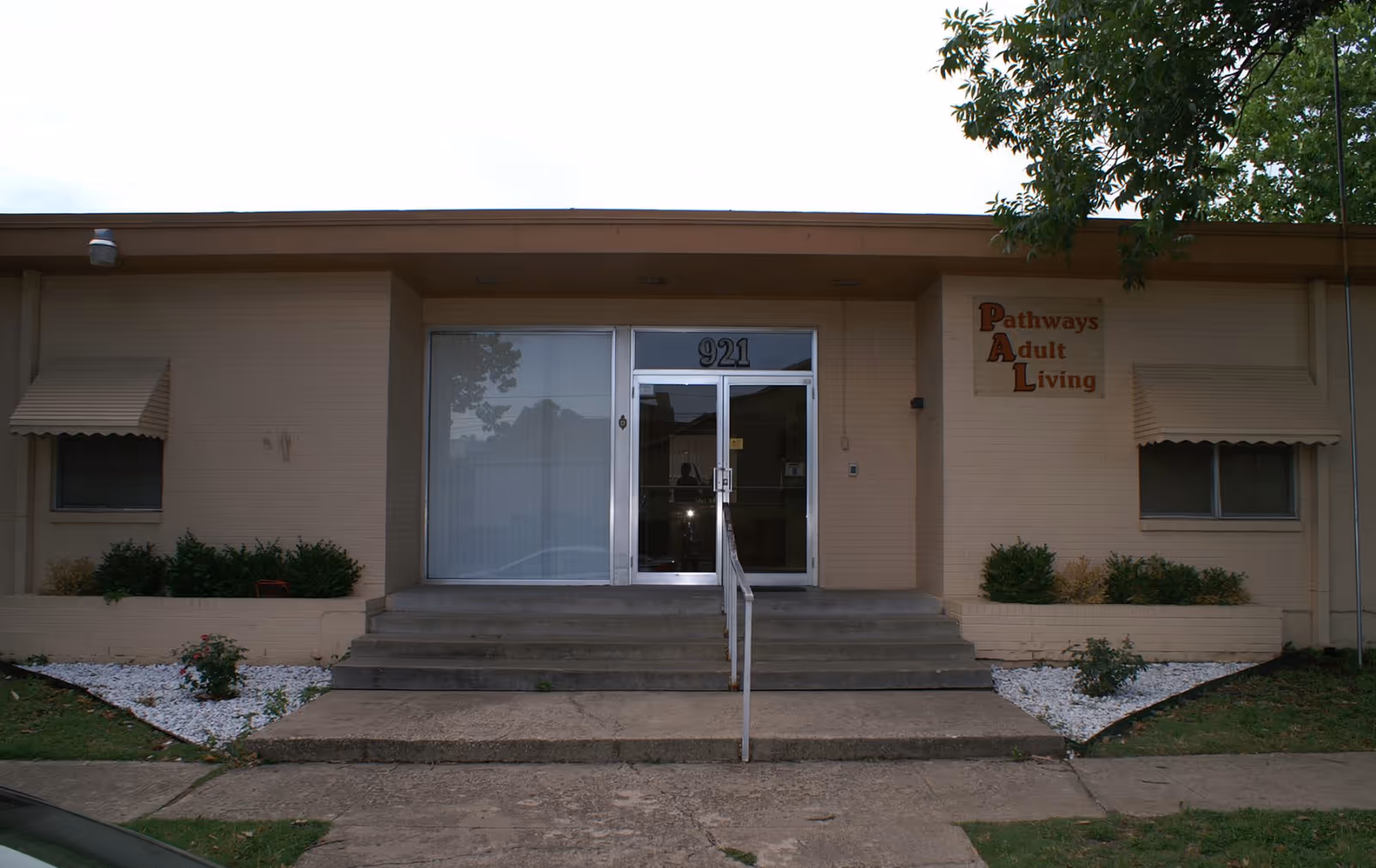 Front entrance of a single-story beige building with steps, a glass door numbered 921, and a sign reading 'Pathways Adult Living'.