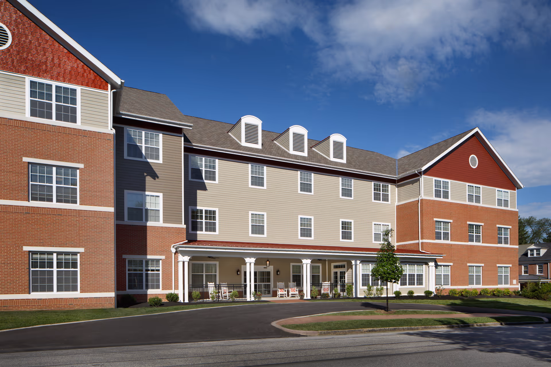 A modern senior living facility with brick and beige siding, front entrance, and manicured landscaping.