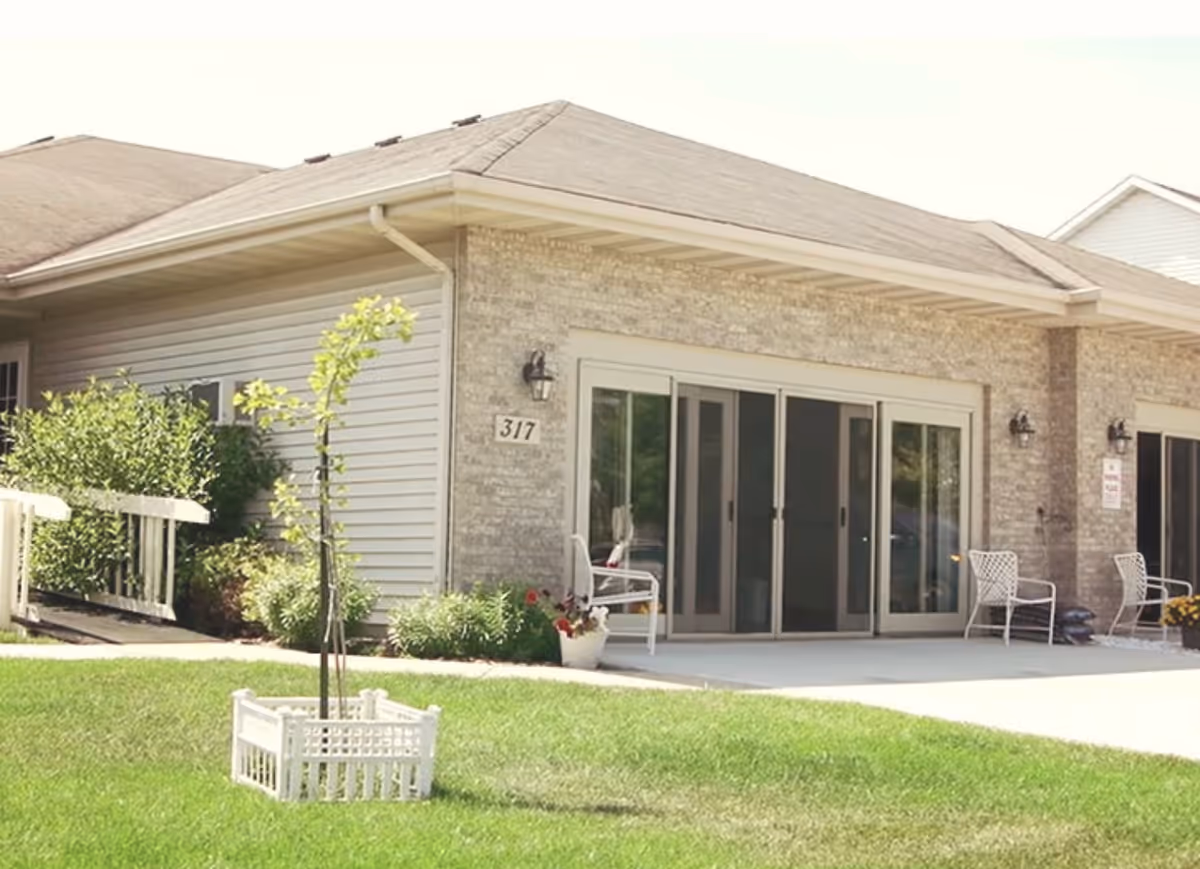 Exterior of Sonrisas Assisted Living with glass doors, chairs, and manicured lawn.