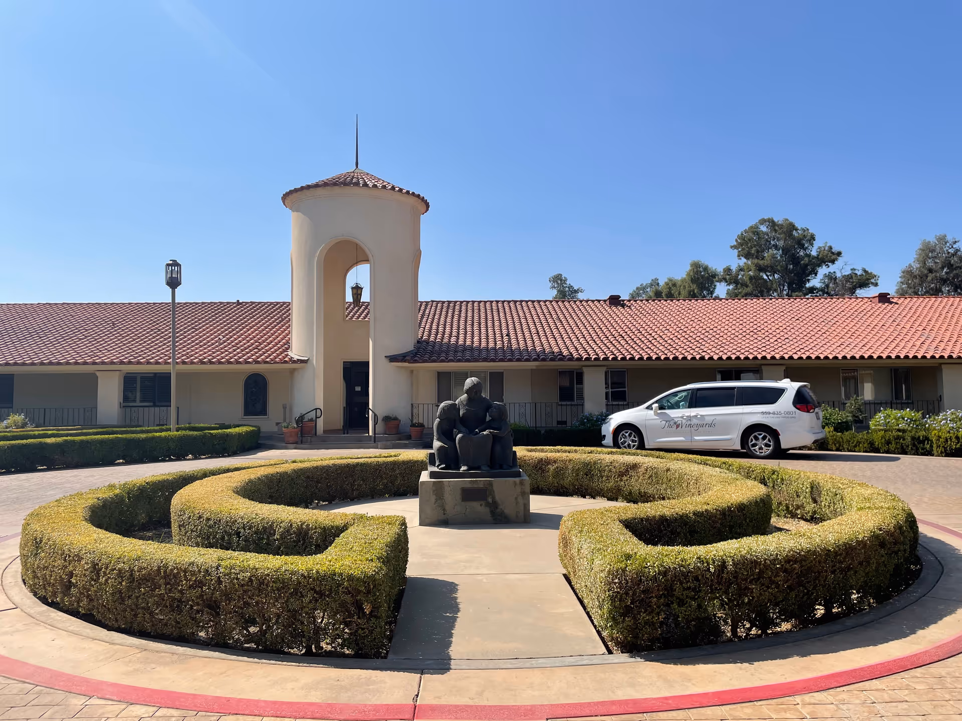 Exterior view of The Vineyards building with a circular hedge and statue centerpiece.