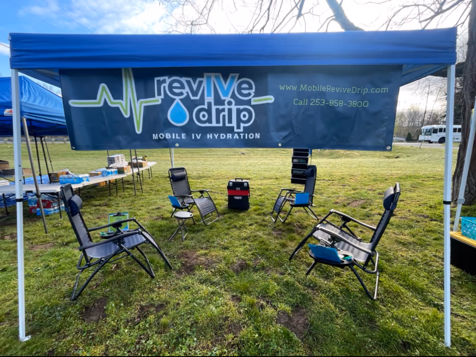 Outdoor tent with banner reading Revive Drip and foldable chairs arranged in a circle.