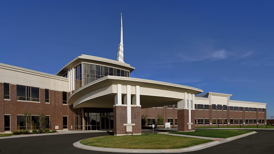 Modern brick outpatient clinic with curved entry canopy and spire against blue sky.