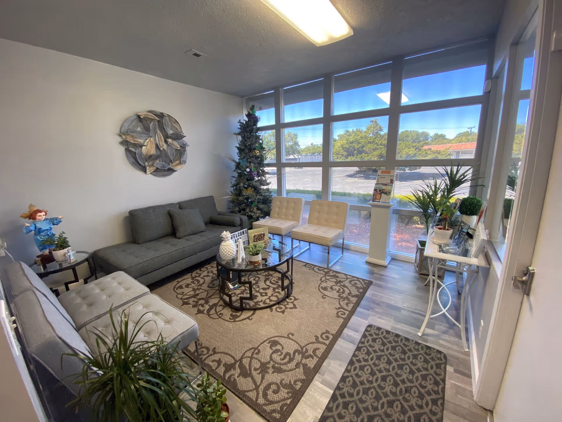 Bright lounge area with sofa, chairs, a coffee table, large windows, and a Christmas tree.