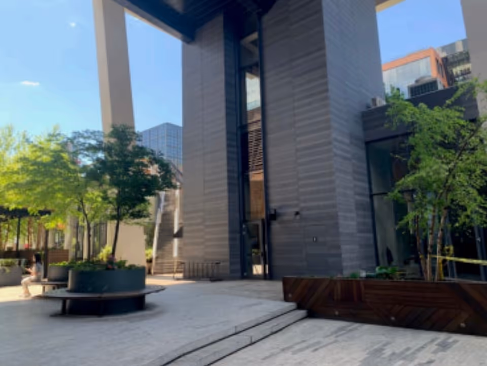 Outdoor courtyard of a modern building with benches, trees, and stone pathways.