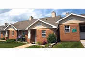 Brick facade of Normandie Ridge senior living facility with manicured lawn and a green sign.
