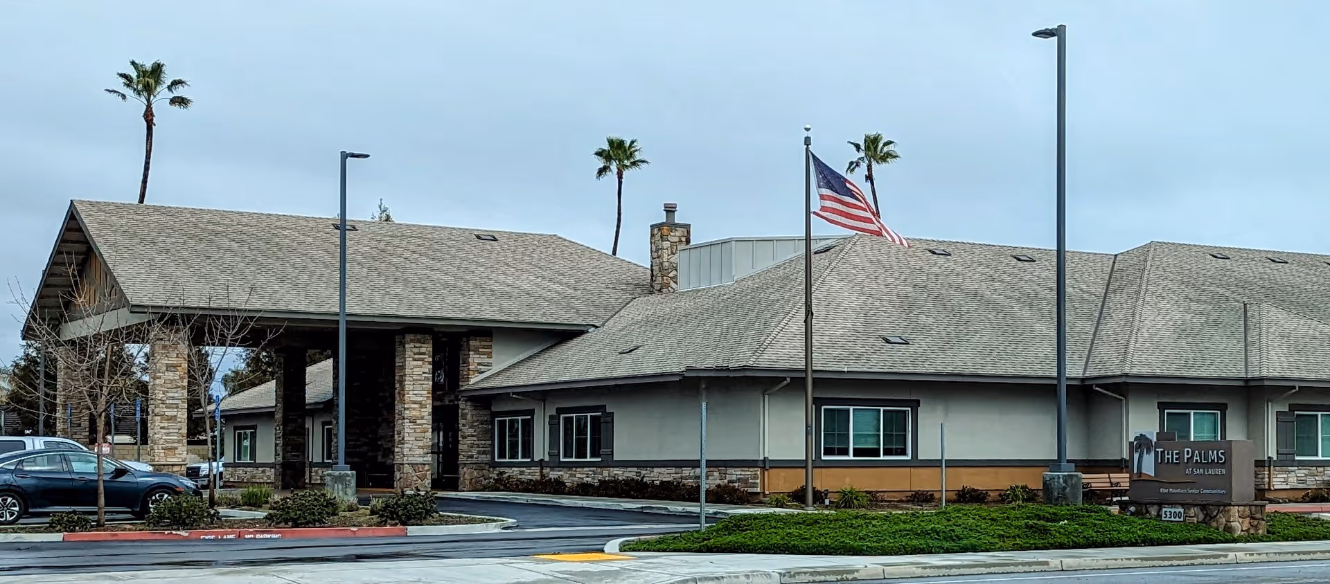 Exterior view of a senior living facility with a covered entrance and palm trees.