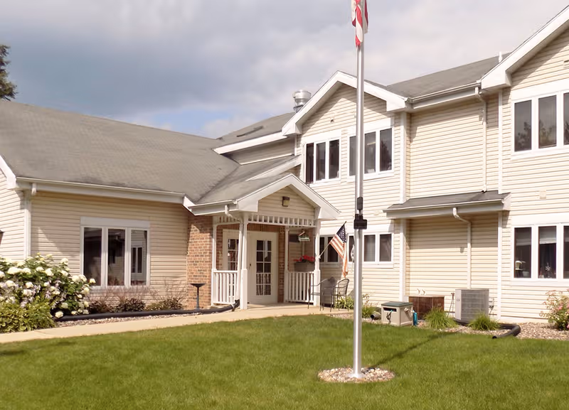 Exterior view of Dimensions Living Stoughton building with entrance, lawn, and flagpole.