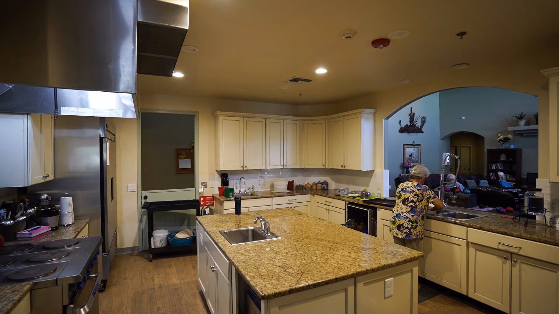 Spacious granite kitchen with an island, cabinets, and a resident at the counter.