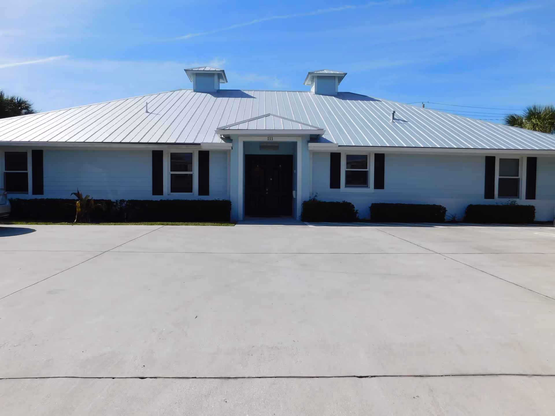 Castlewood ALF exterior: single-story blue building with metal roof and wide concrete driveway.