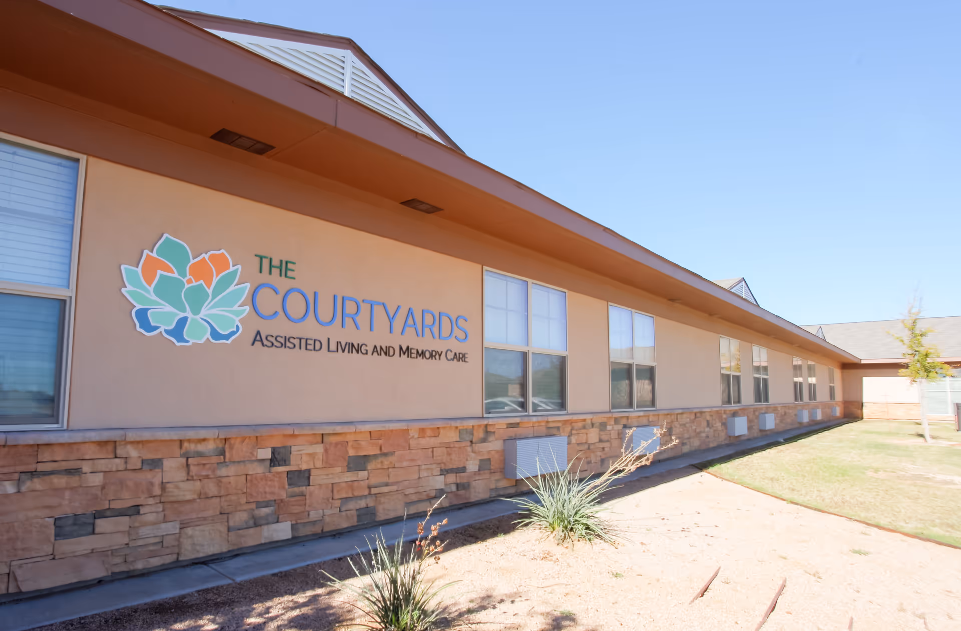 Exterior view of The Courtyards Assisted Living and Memory Care single-story building with its logo and row of windows.