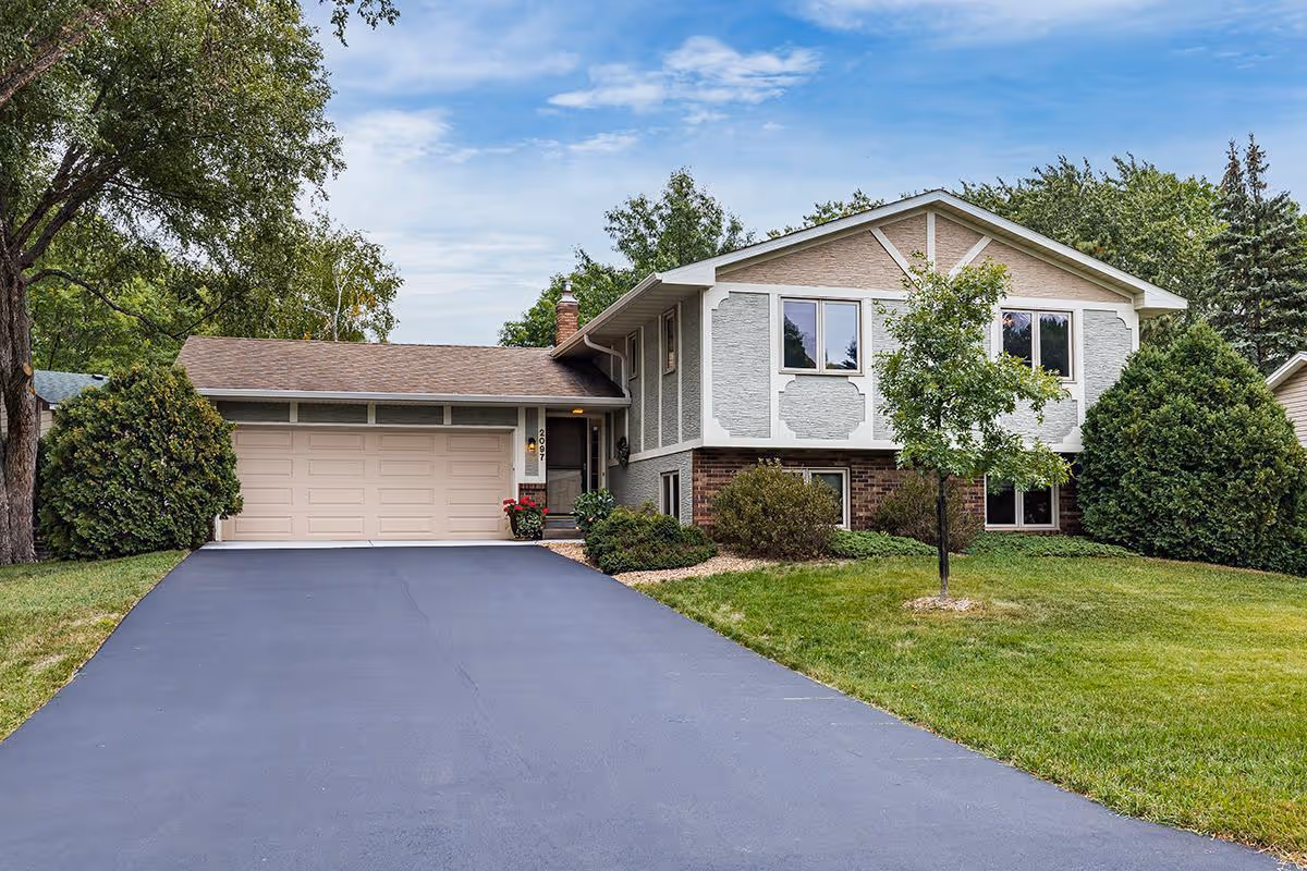 Two-story house-style senior living facility exterior with driveway and trees.