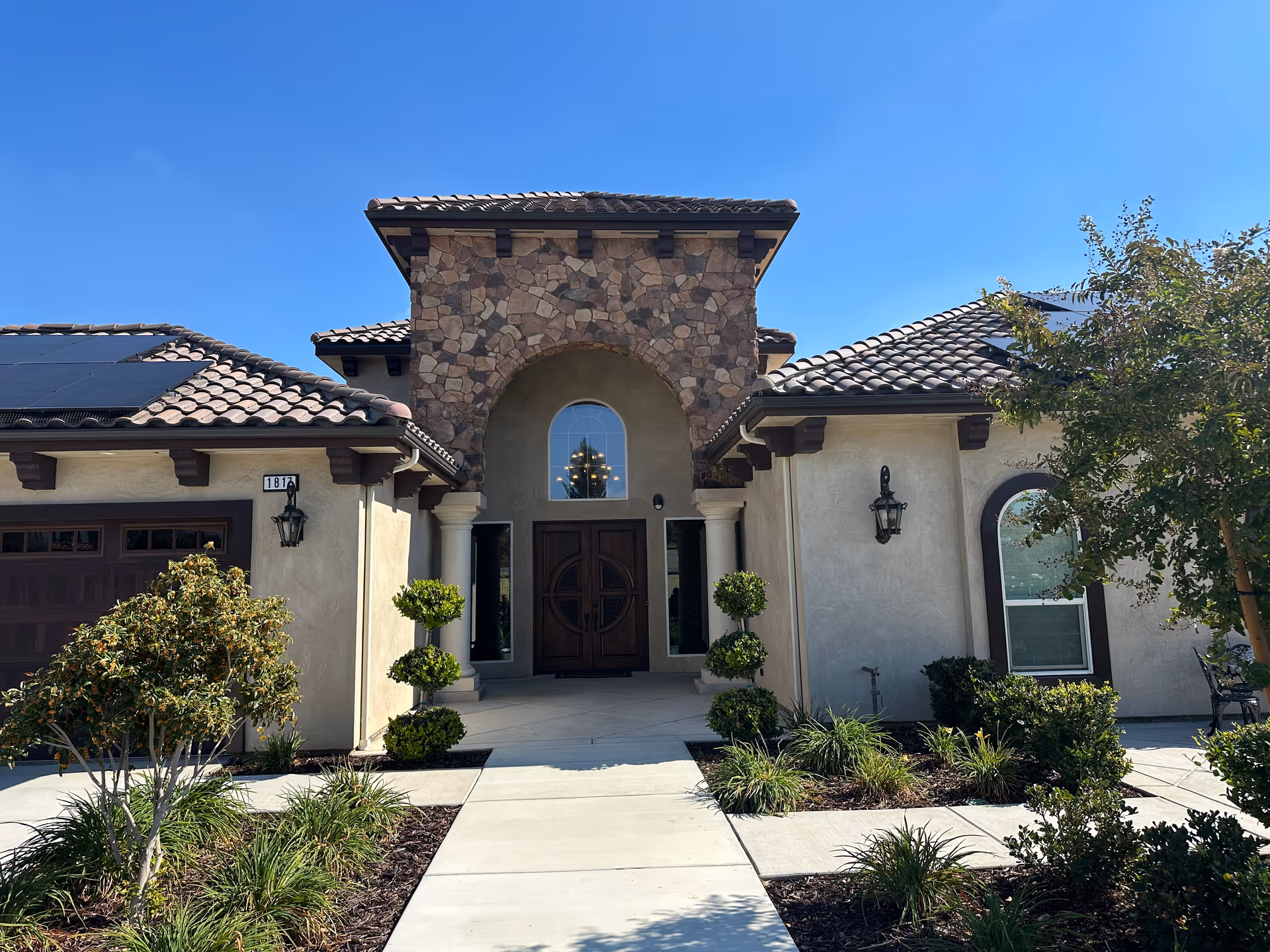 Front entrance of a Mediterranean-style senior living facility with stone arch and landscaping.