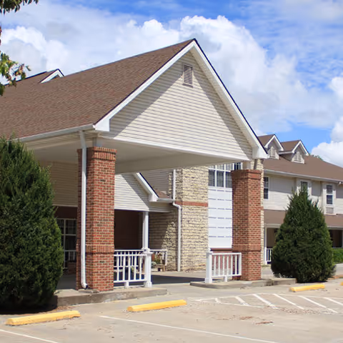 Exterior view of a senior living facility front entrance with brick columns and a covered porte-cochere.