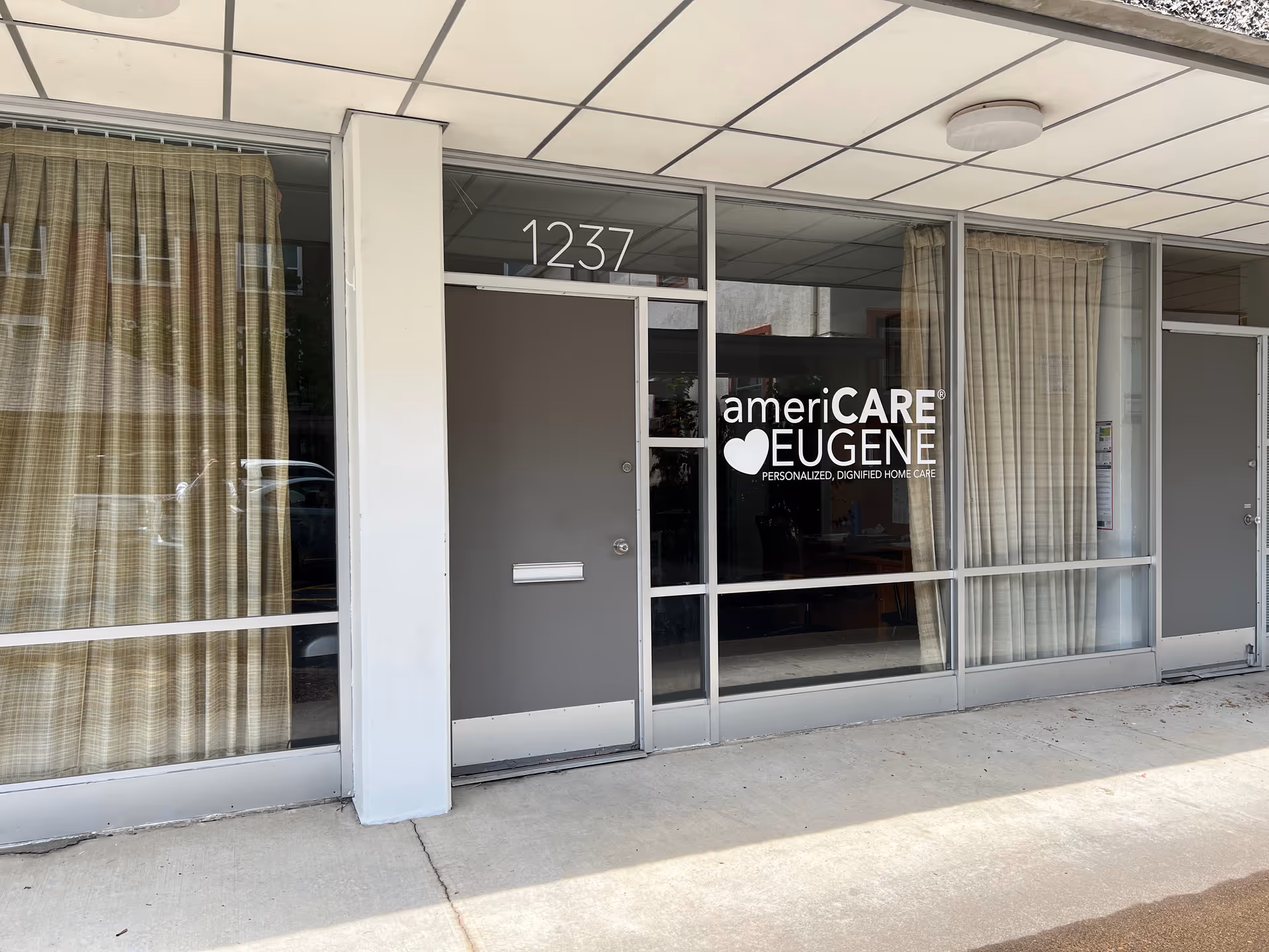 Exterior storefront of americare Eugene with glass windows, curtains, and a grey entrance door.