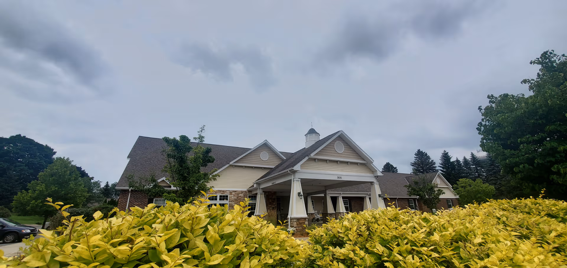 Exterior view of Bickford of Okemos with a covered entrance and shrubs in foreground.