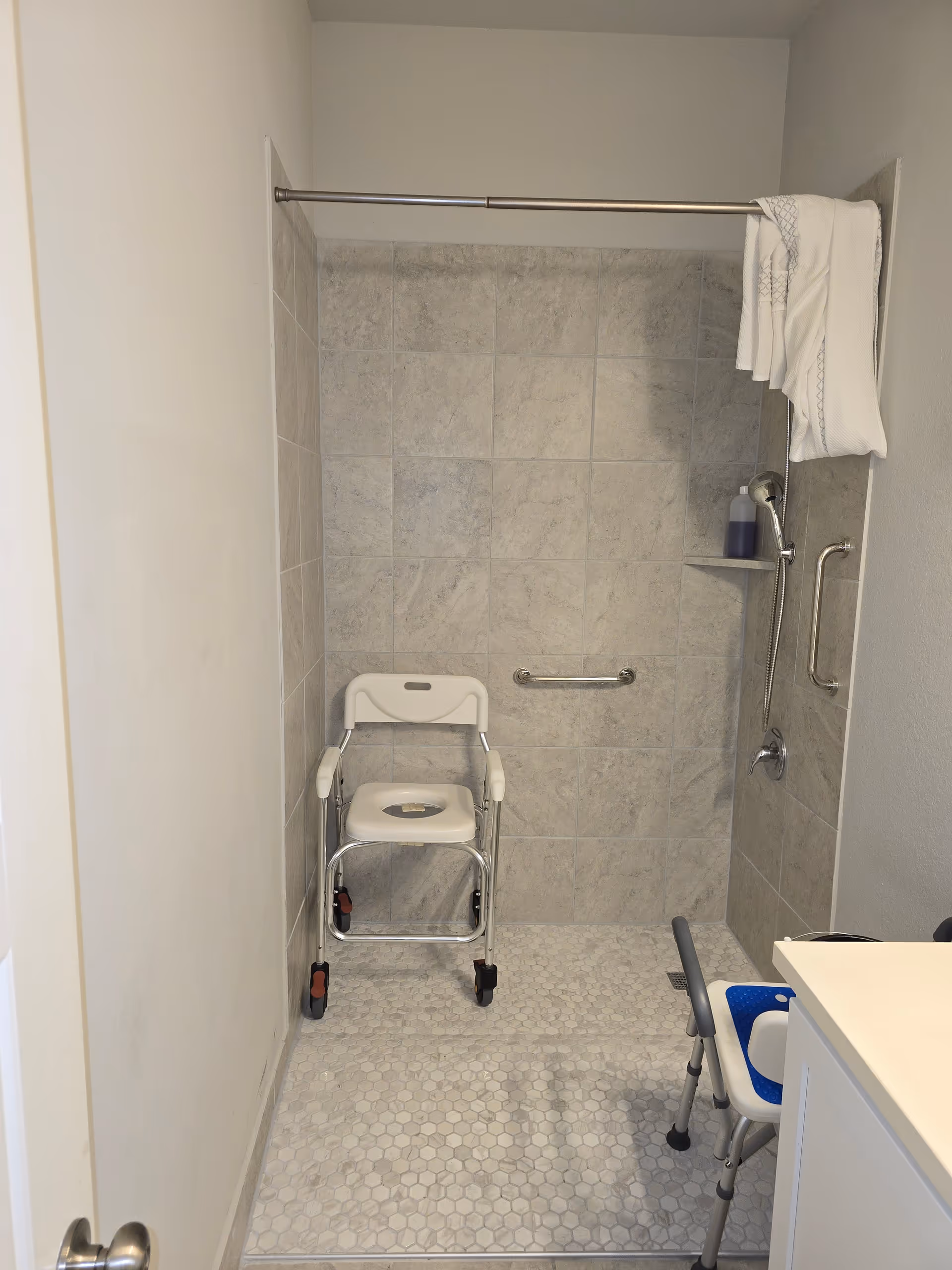Interior bathroom with tiled shower, safety grab bars, and a mobile shower chair for residents.
