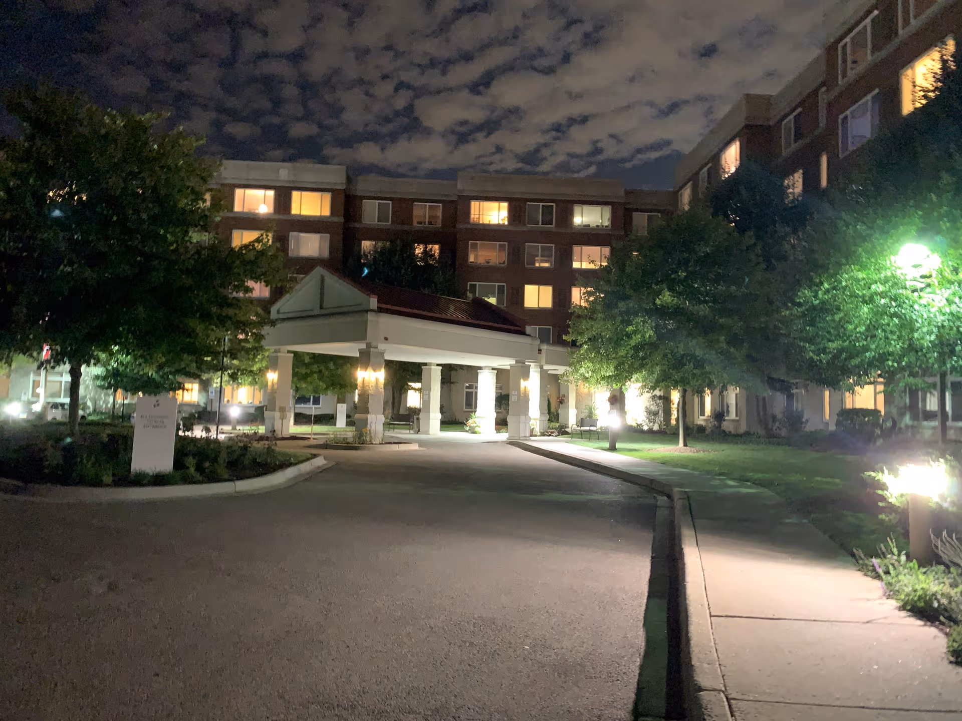 Night exterior of Brookdale Northbrook showing illuminated entrance canopy and surrounding trees.