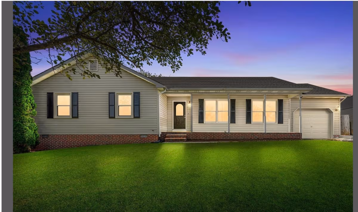 Single-story house exterior with a front lawn, porch, and attached garage at dusk.