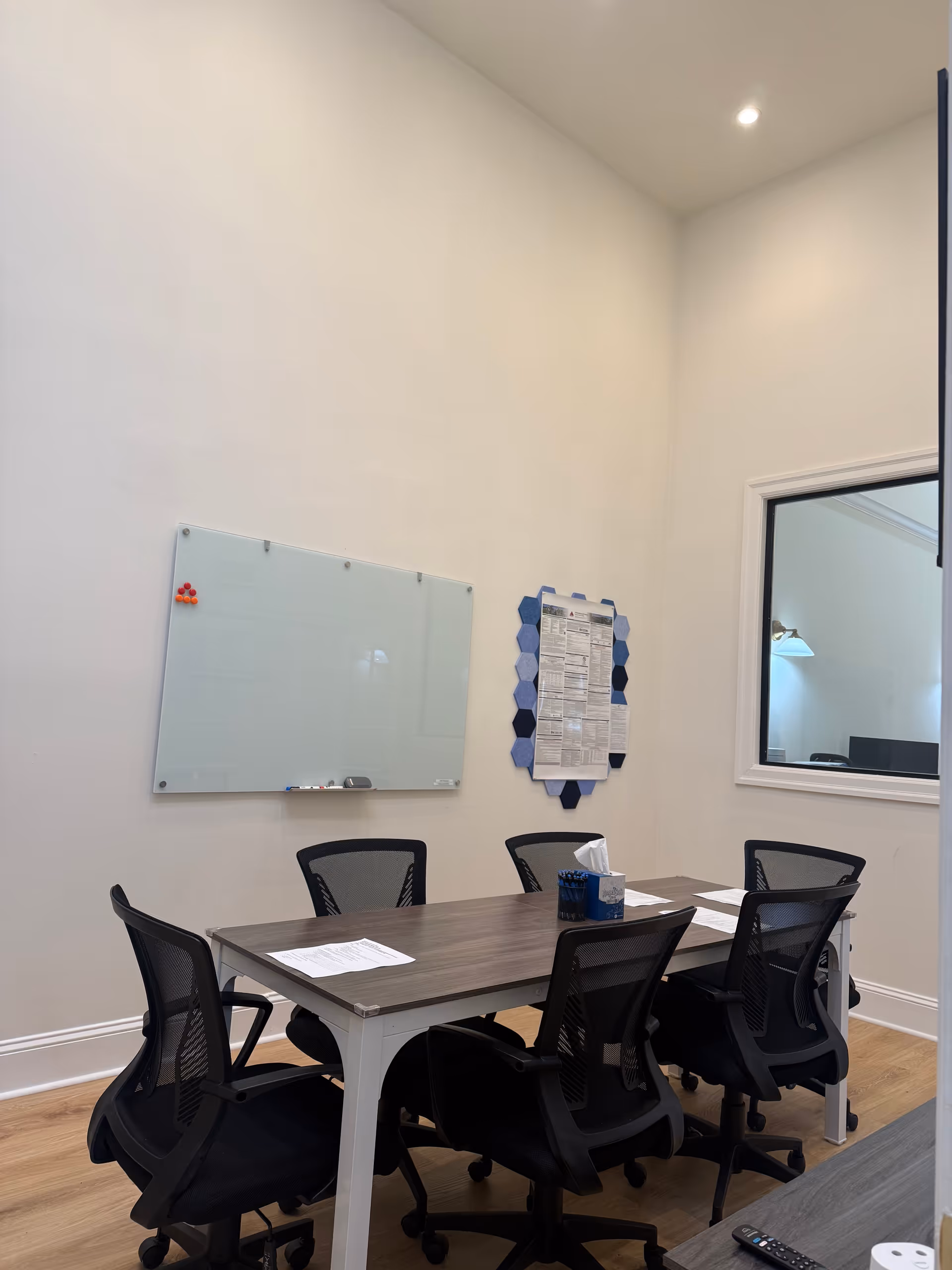 A small conference room with a dark wood table, chairs, whiteboard, and bulletin board.