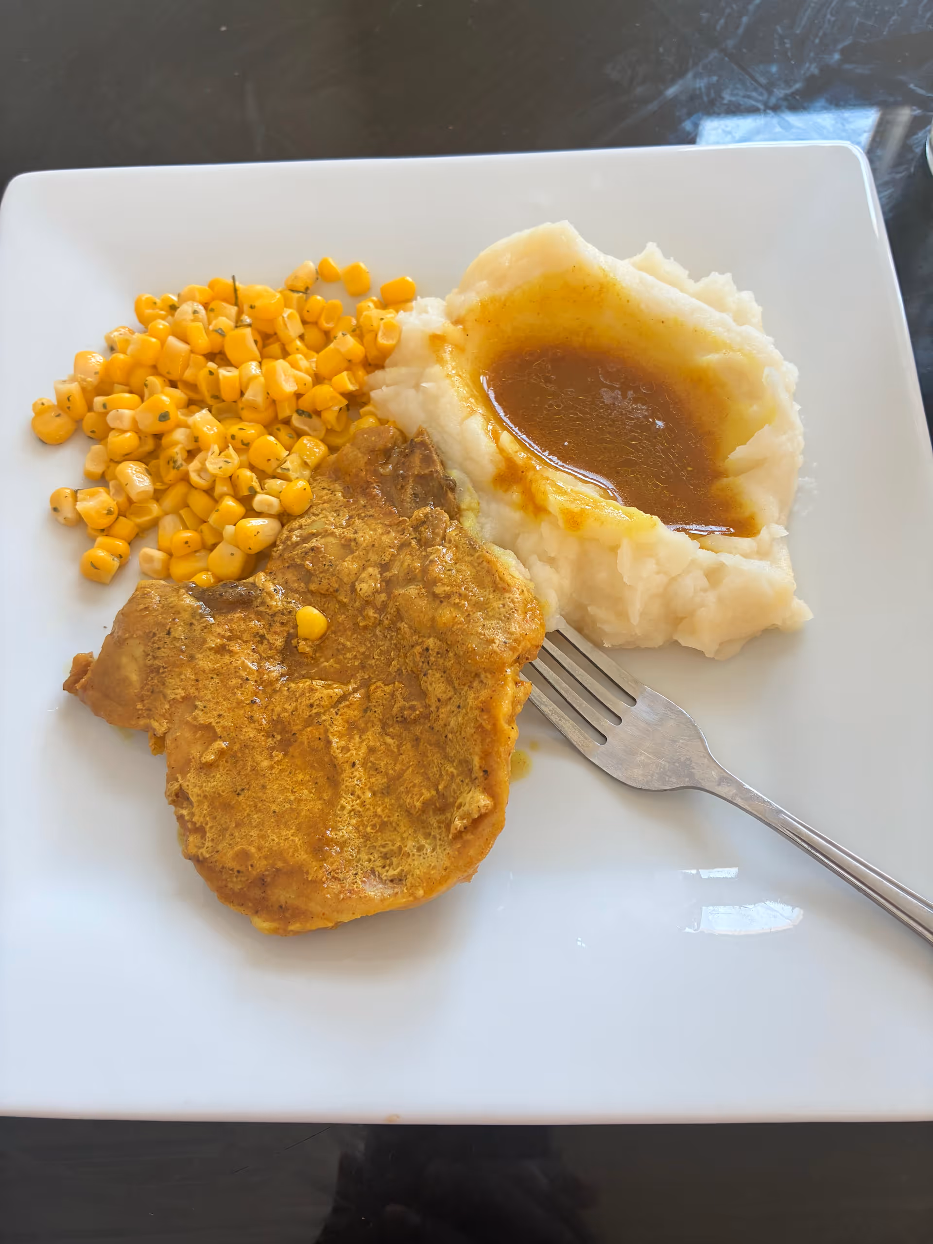 Plate features corn, mashed potatoes with gravy, and a breaded meat patty.