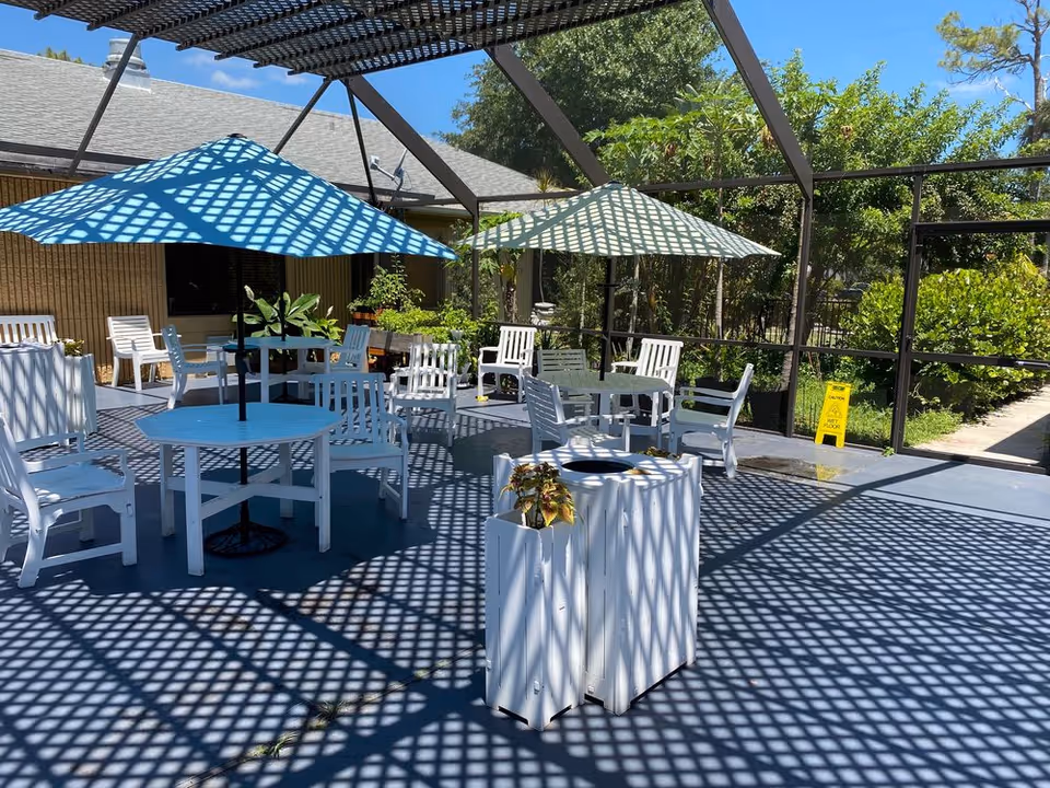 Outdoor patio of Menorah House with white tables, chairs, and shaded lattice canopy.