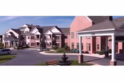 Exterior view of a pink senior living campus with a central fountain in a courtyard.