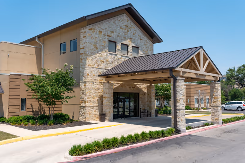 Exterior view of The Enclave senior living facility with stone facade and covered entrance.