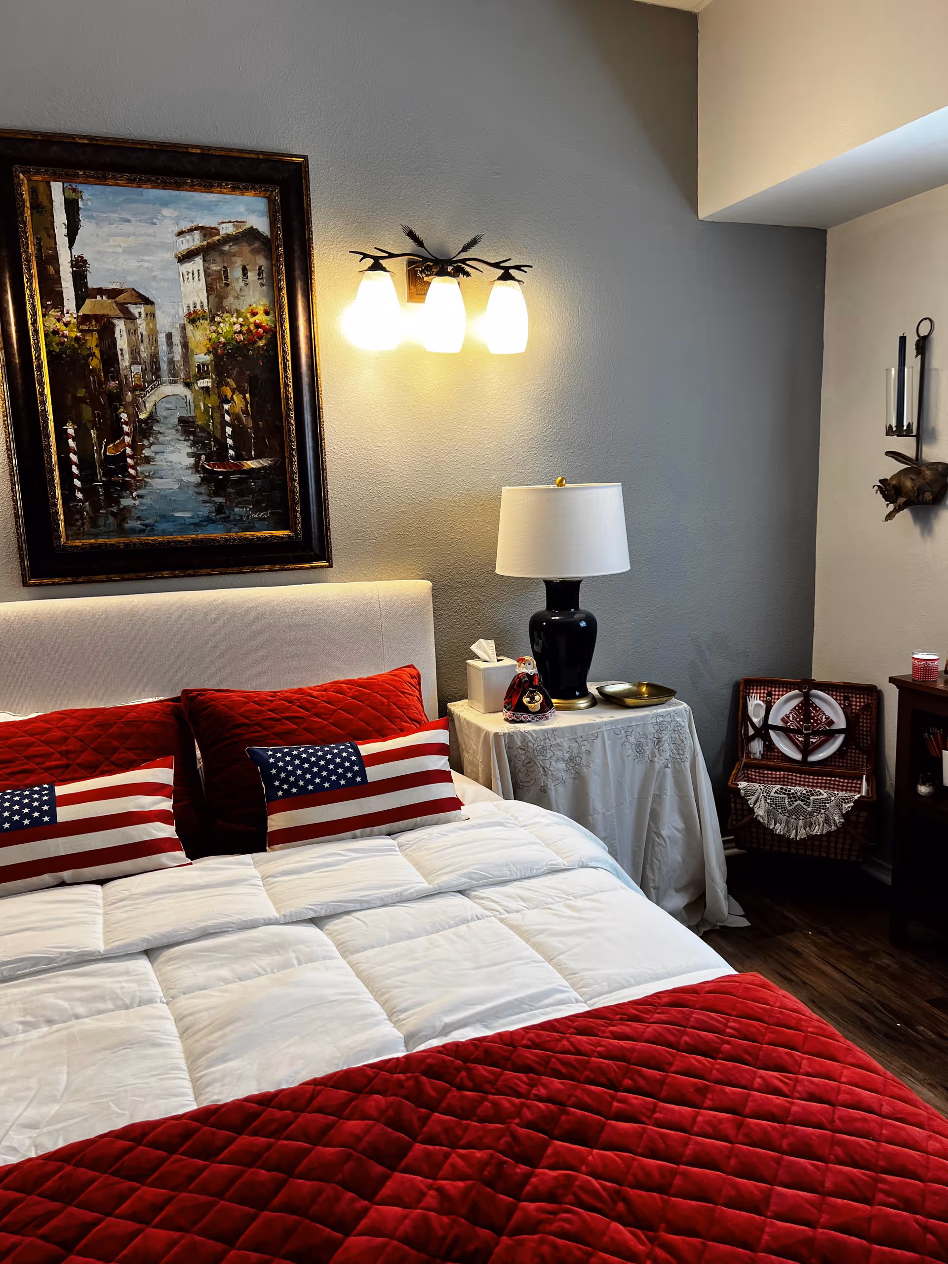 A neatly made bed with red and white bedding, American flag pillows, and a bedside table.