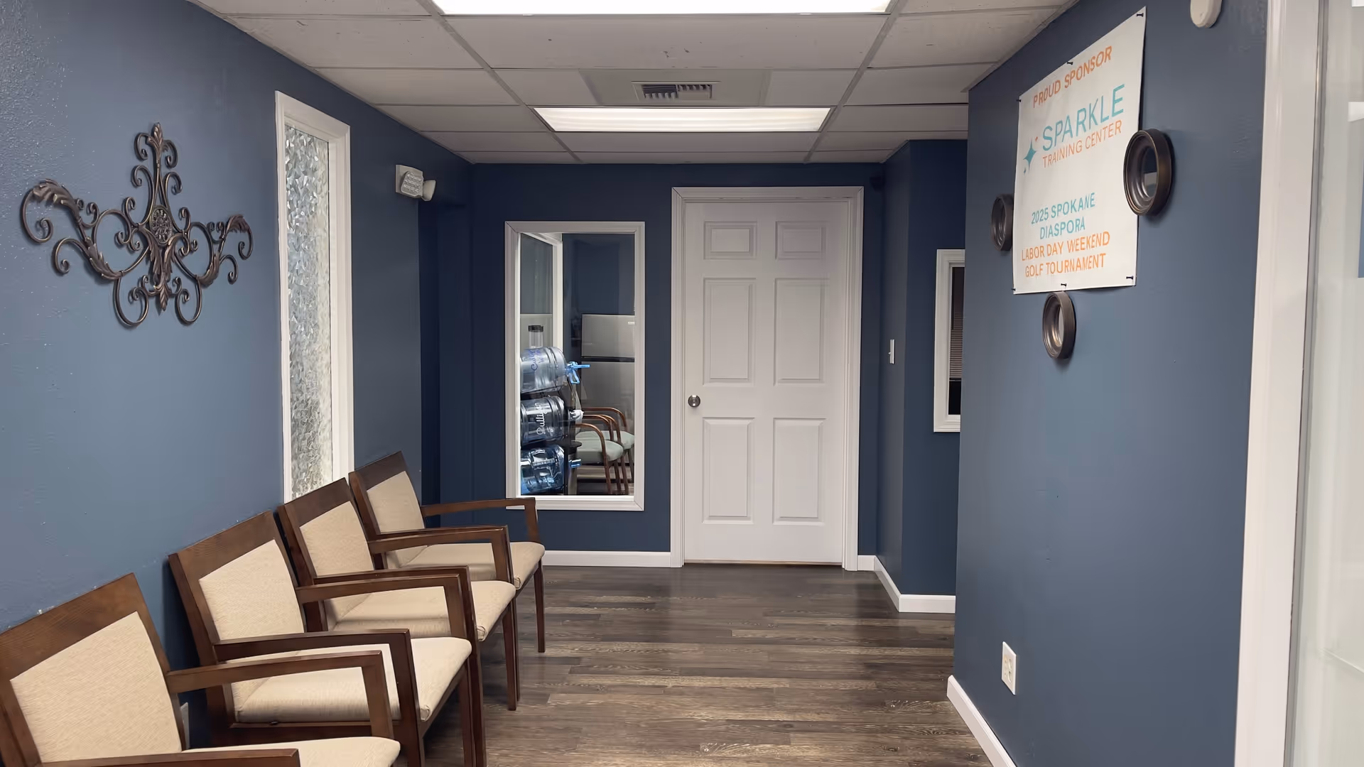 Blue hallway with wooden chairs along the wall, a white door, and Sparkle Training Center sign.