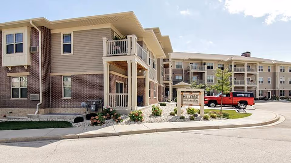 Exterior view of Hillcrest Apartments complex with signage, landscaping, and parked vehicles.