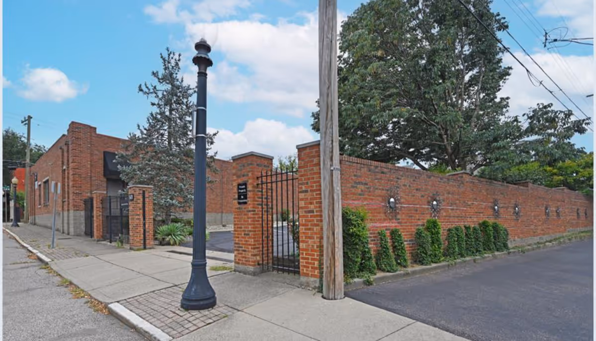 Brick building exterior with a gated entry, sidewalk, lamppost, and a brick wall along the street.