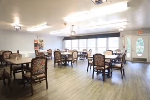 A spacious senior living dining hall with multiple tables and floral chairs.