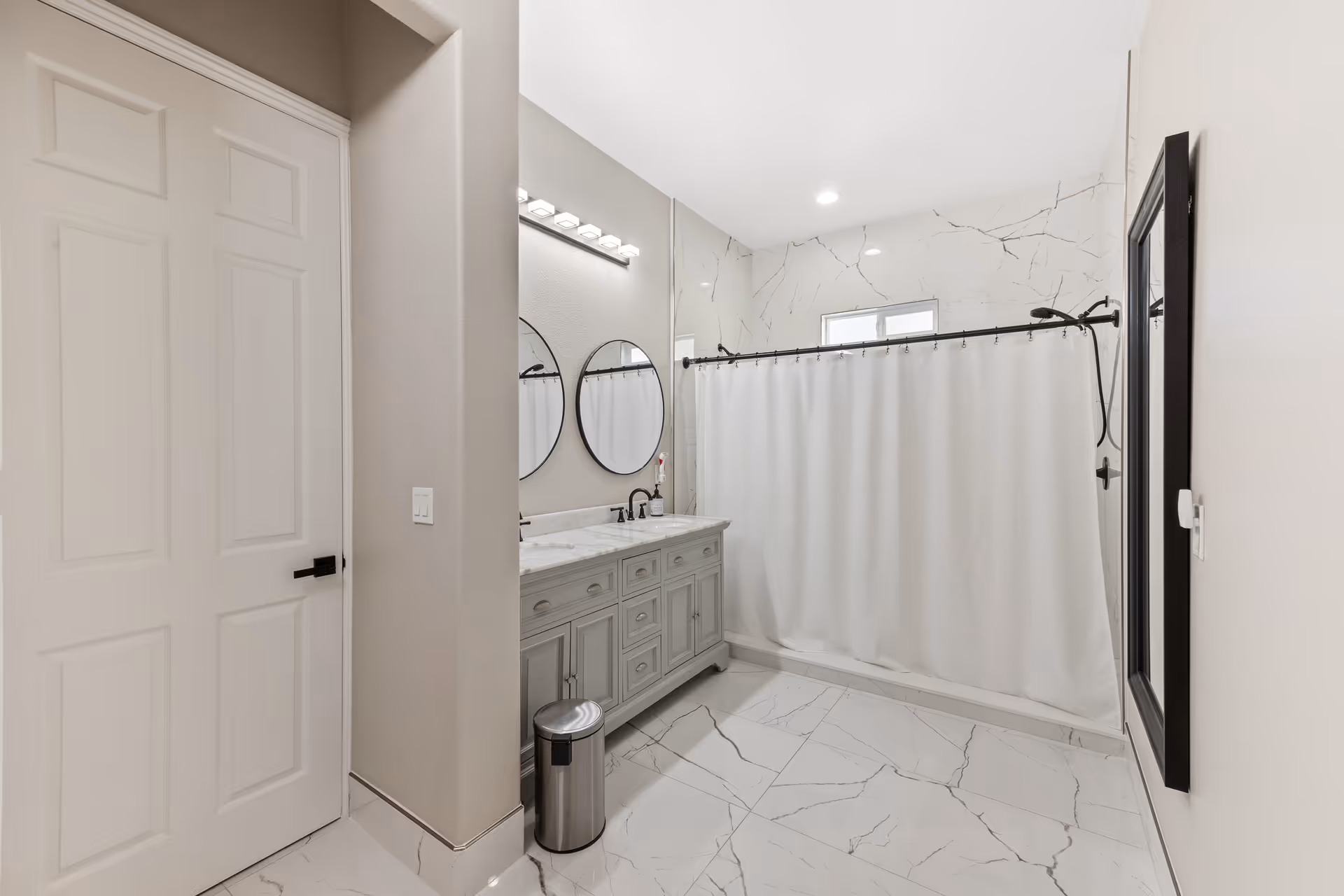 Bright bathroom with double vanity, round mirrors, and marble-tiled shower.