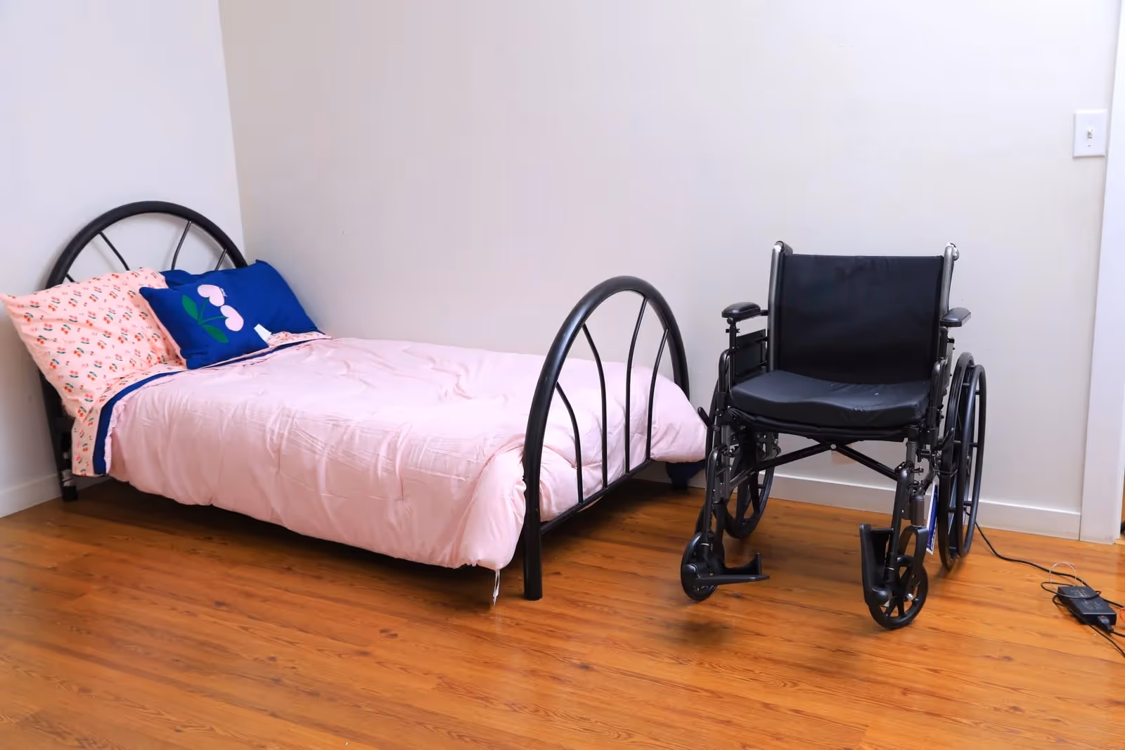 Bedroom with a metal bed frame, pink bedding, and a wheelchair nearby