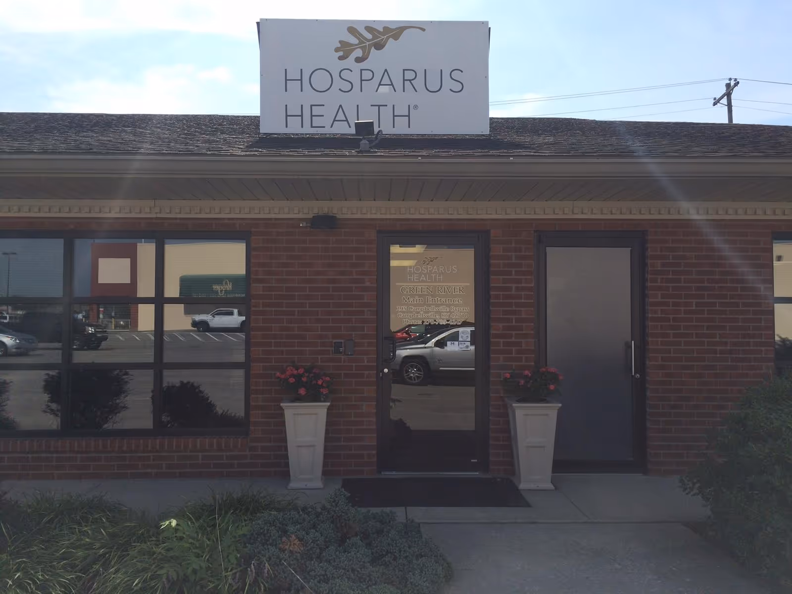 Front of brick building displaying Hosparus Health sign and glass door.
