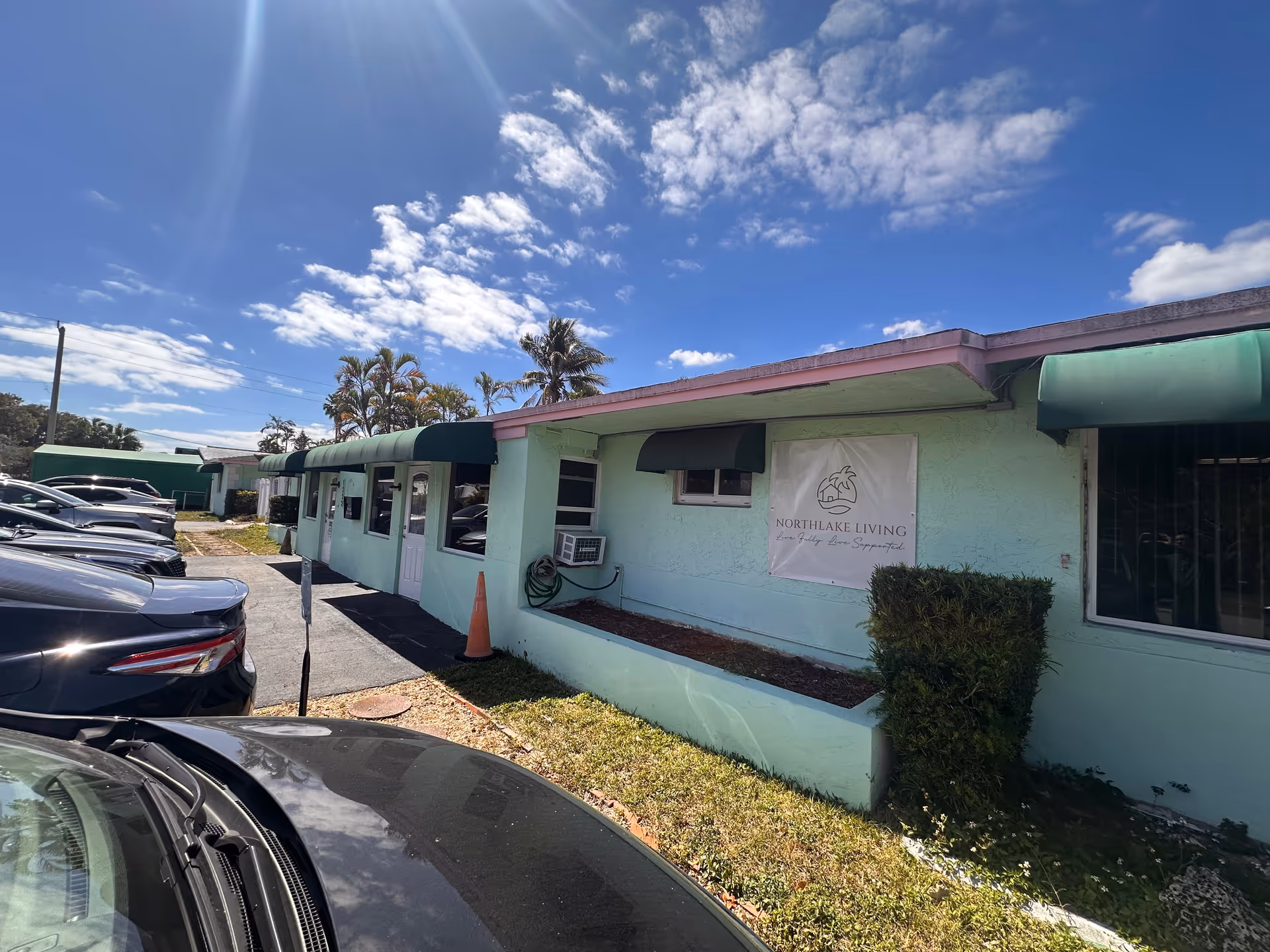 Mint-green single-story retirement home exterior with awnings and parked cars.