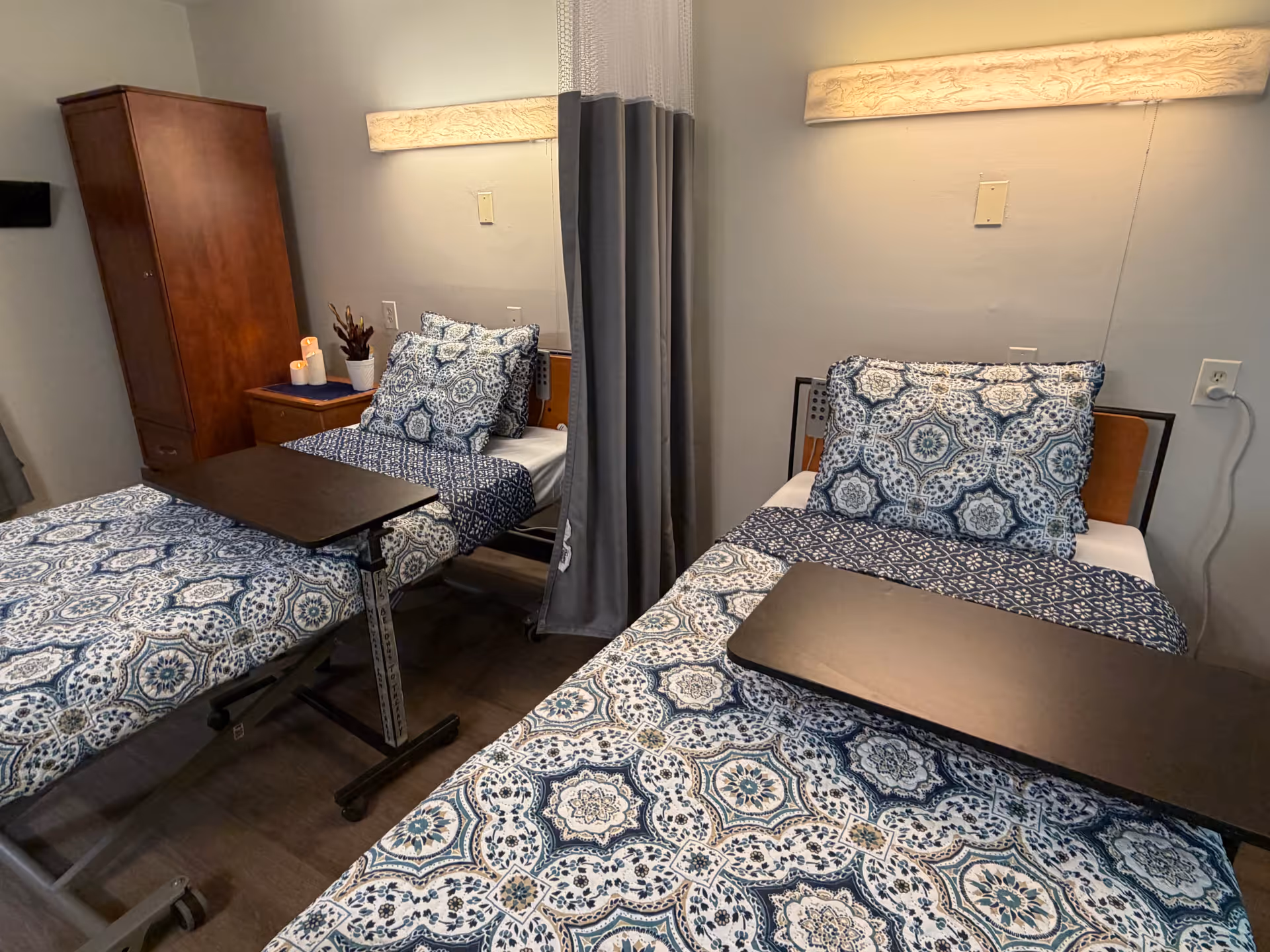 Two twin beds with blue patterned linens and a privacy curtain in a shared room.